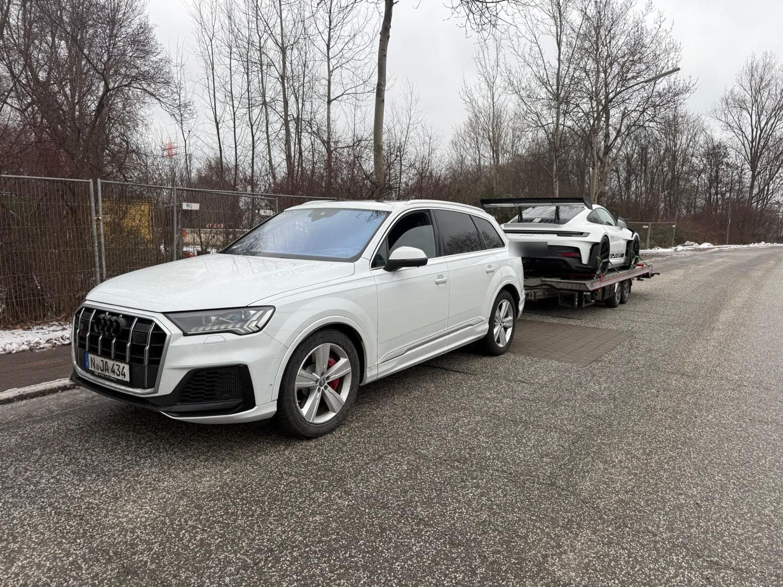 Weißer Audi SQ7 mit Autotransportanhänger und Porsche 911 GT3 RS im Winter