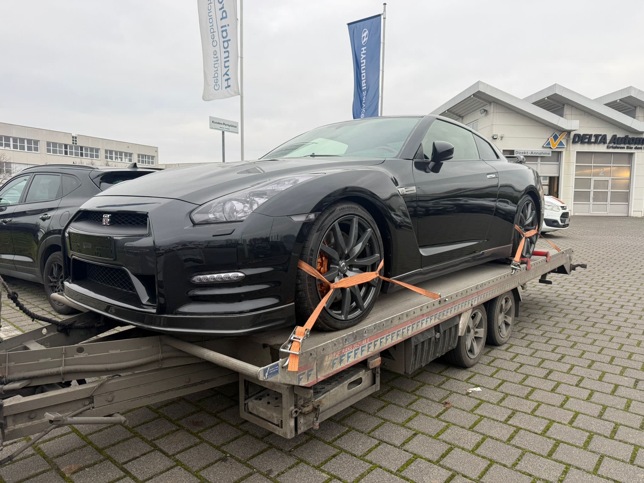 Schwarzer Nissan GT-R auf Autotransportanhänger vor einem Autohaus