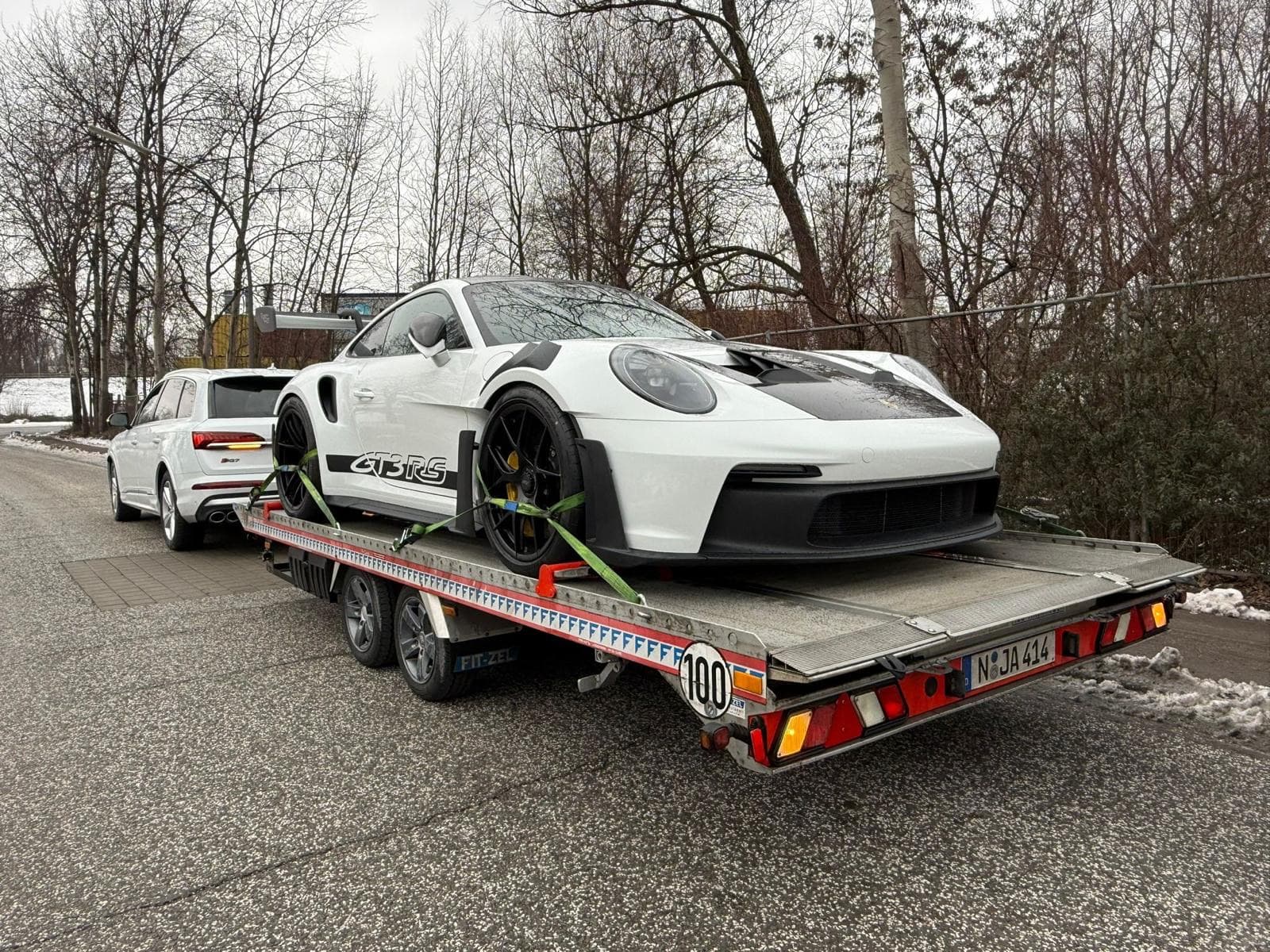 Weißer Porsche 911 GT3 RS auf offenem Autotransportanhänger hinter Audi SQ7